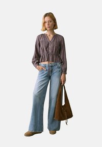 Lyslilla bluse med lange ærmer og blomsterprint, med snor i taljen, parret med lysblå vide jeans og en brun suedestrop taske.