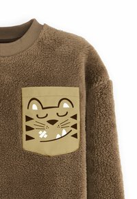 Sudadera de forro polar marrón con un bolsillo color beige claro que presenta un diseño de cara de gato impreso en marrón oscuro y acentos en blanco.