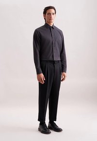 Koolstofkleurig overhemd met knopen en een subtiele textuur, gecombineerd met op maat gemaakte zwarte broek en zwarte leren schoenen, staand tegen een neutrale achtergrond.