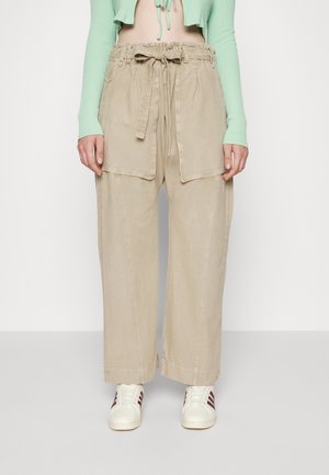 Pantalones beige de pierna ancha con bolsillos con solapa en la parte delantera y cinturón de tela atado a la cintura, combinados con zapatillas blancas y un top cropped de manga larga verde menta.