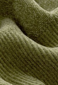 Olivzaļš kordžūrijas audums ar mīkstu tekstūru un izteiktām vertikālām ribām, radot viļņainu izskatu ar smalkām detaļām.