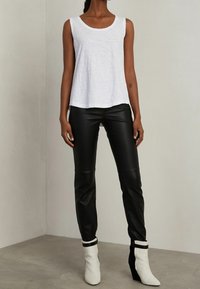 Bílý bezrukávový top s výstřihem do lodičky v kombinaci s černými koženými přiléhavými kalhotami a černobílými wedge kotníkovými botami s detailním zapínáním.