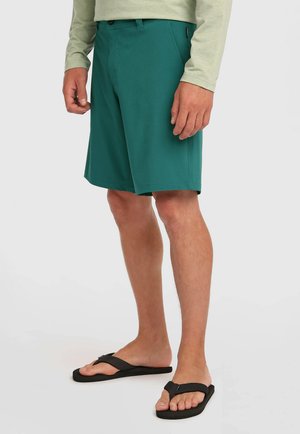 Pantaloncini turchesi realizzati in tessuto leggero, con taglio dritto, passanti per cintura e tasche laterali. Abbinati a infradito nere.