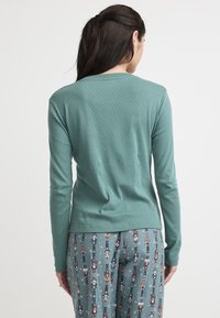 Langarmshirt in teal met een subtiele textuur en ronde halslijn, gedragen met gestreepte pyjamabroek met het ontwerp van notenkrakers.