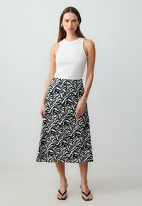 Witte mouwloze top gecombineerd met een zwart-witte rok met een bladetekening en teal accenten, knie-lang, en een gladde textuur.