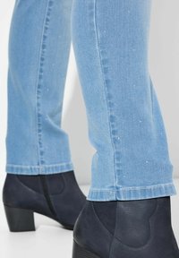 Vaqueros de denim azul con embellishments sutiles, combinados con botines negros de tacón con una textura suave y detalle de cremallera.