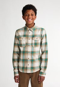 Košile s límečkem v károvaném vzoru s kombinací tyrkysové, hnědé a krémové barvy. Obsahuje dvě náprsní kapsy a zapínání na knoflíky.