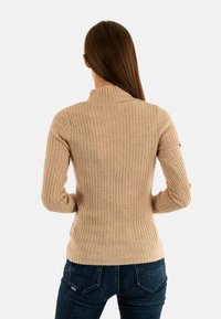 Maglione beige a coste con colletto alto e maniche lunghe. Il materiale sembra morbido e ha un design aderente. Motivo testurizzato su tutto il capo.