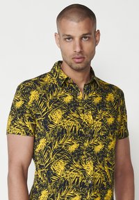 Camasa cu maneci scurte, cu un fundal negru si un model de frunze tropicale galbene, cu inchidere cu butoni si guler standard.