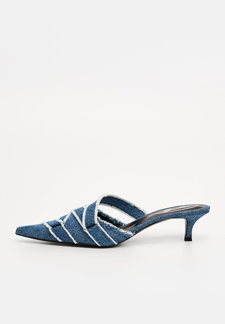 Mule in denim con punta affusolata, caratterizzati da cuciture bianche e cinturini intrecciati. Il tacco sottile e la texture morbida conferiscono un aspetto casual.