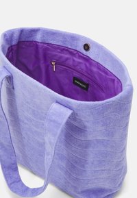 Sac fourre-tout en tissu violet clair avec surface texturée, doublure violette unie. Comprend une poche intérieure zippée et des détails de couture.