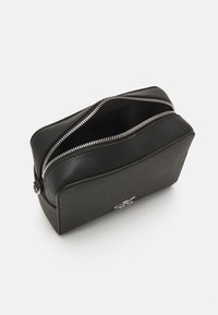 Borsetta in pelle nera con superficie texture, chiusura con zip e un logo argentato sul davanti. L'interno è non foderato e spazioso.