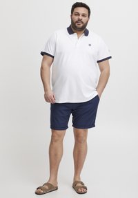 Hvit polo skjorte med marineblå krage og mansjetter, kombinert med marineblå shorts. Brukt med brune sandaler. Uformell, lett stoff.