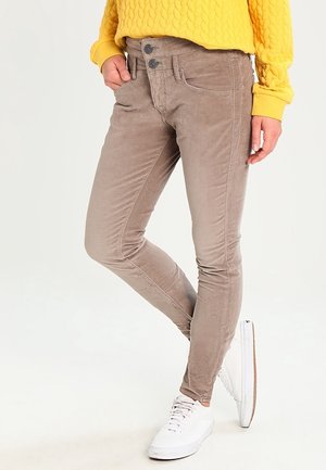 Person wearing beige slim-fit pants with double button closure, yellow textured sweater, and white sneakers, standing with one leg crossed.