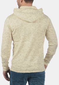 Helle beige Baumwollkapuzenpullover mit strukturiertem Stoff und Kapuze. Verfügt über lange Ärmel und ein tailliertes Design, von hinten gezeigt.