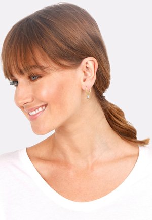 Goldene Hoops mit einem rechteckigen Kristallanhänger. Glatte Metalloberfläche, minimalistisches Design und schlanke Form.