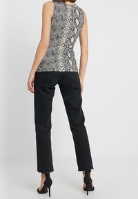 Ärmlös topp med ett ormskinnsmönster i grå och krämfärgad nyanser; kombinerad med svarta jeans med fransar och eleganta klackar.