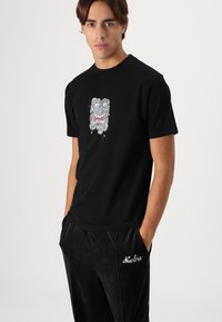 Zwarte katoenen t-shirt met een grafisch ontwerp van een woeste gezicht in wit en rood. Korte mouwen, ronde hals, getailleerde pasvorm.