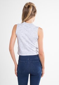 Top gris sin mangas con un cuello alto, que presenta una textura sutil. Combinado con unos vaqueros ajustados de color azul oscuro, que exhiben un diseño clásico de cinco bolsillos.
