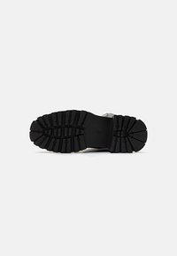 Black rubber shoe sole with deep tread patterns for traction and stability. Smooth edges with circular and angular cutouts for flexibility.