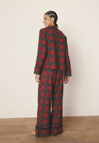 Roter karierter Pyjama-Anzug mit einem kragenlosen Jäckchen und weitem Hosenbein. Hergestellt aus weichem Stoff mit blauen und grünen Akzenten und einem lässigen Schnitt.