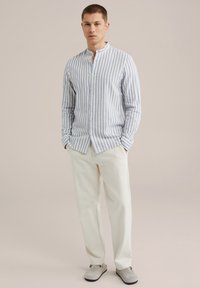 Camicetta a righe blu chiaro e bianco a maniche lunghe con colletto alla cinese, abbinata a pantaloni beige e scarpe slip-on grigie.
