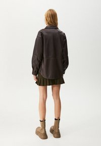 Brun läder skjortjacka med sänkta axlar, i kombination med en mörkgrön veckad kjol och kraftiga beige ankelstövlar. Enkel, stilren design.