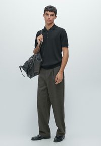 Polo shirt noir, pantalons à carreaux ajustés et chaussures noires brillantes. Sac en cuir gris avec des détails zippés, porté en bandoulière sur l'épaule gauche.