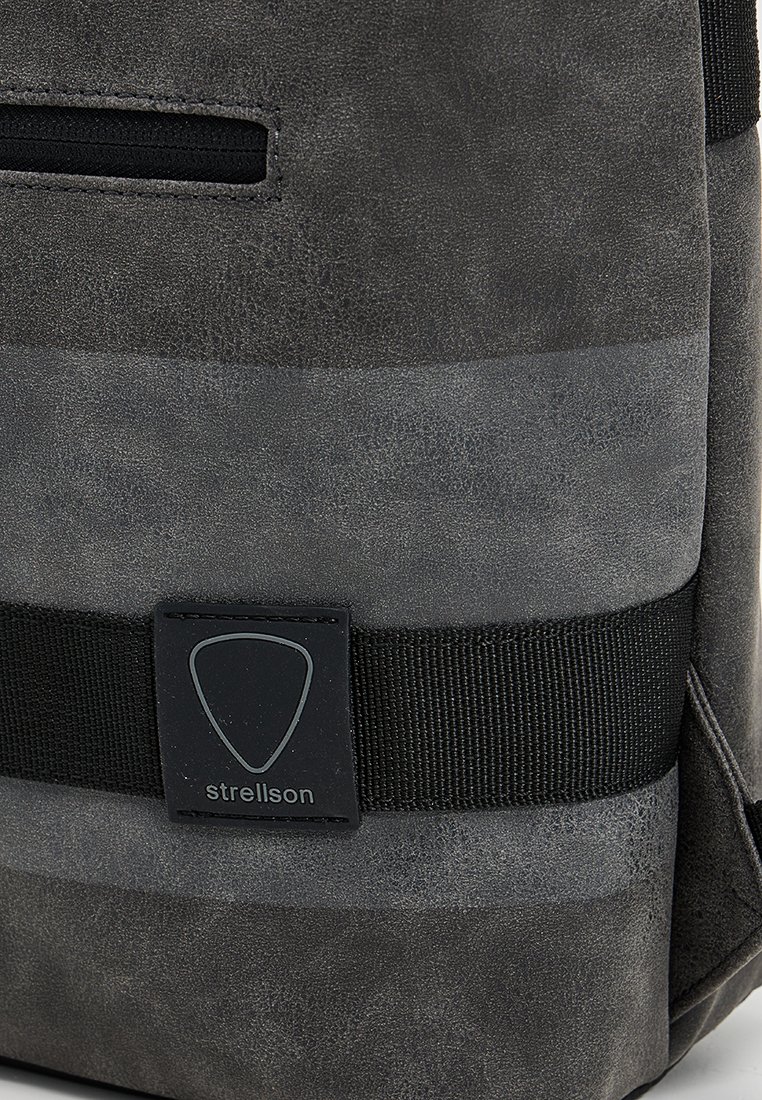 Zaino in pelle grigia con una striscia orizzontale a contrasto, una tracolla in tessuto nera e una patch logo con bordi arrotondati.