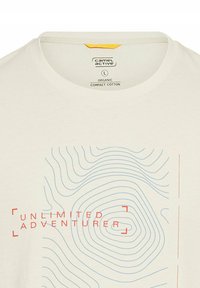 Hvid økologisk bomulds t-shirt med et blåt topografisk linjemønster og rød tekst, der siger "UNLIMITED ADVENTURER." Rund halssdelse.