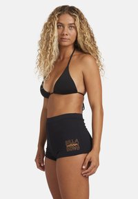 Top bikini nero con spalline sottili e pantaloni corti a vita alta abbinati, caratterizzati dal testo colorato "BILLA BONG". Tessuto liscio, design aderente.
