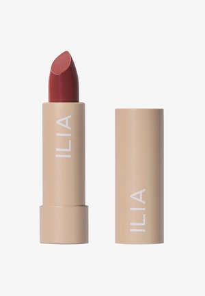 ILIA lippenstift in een beige tube met witte tekst. De lippenstift heeft een diepe rode kleur met een gladde, ronde punt en een glanzende afwerking.