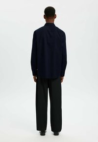 Chemise bleu marine à boutons avec manches longues et coupe droite, associée à un pantalon large noir. Tissu lisse, design minimaliste.