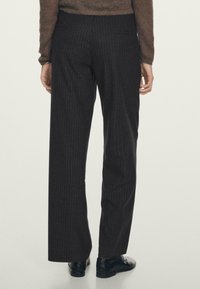 Pantaloni neri a righe con design a gamba dritta, dotati di due tasche posteriori e un tessuto liscio e strutturato. Indossati con scarpe scure.