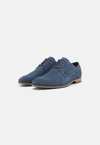 Zapatos de vestir de ante azul marino con un acabado suave, punta redondeada y suela de goma color canela. Presentan un diseño de cordones y acentos laterales texturizados.