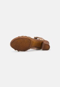 Sandale en cuir marron avec un talon semblable à du bois, dotée d'une semelle texturée et d'ornements métalliques décoratifs le long des lanières.