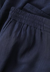 Pantalon bleu marine en gros plan montrant un tissu texturé et une taille élastique avec des coutures froncées et une passoire pour ceinture.