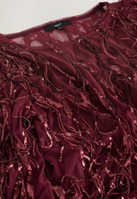 Burgundy top featuring a sheer fabric with hanging sequined accents, creating a textured appearance. Tag reads "NEXT."