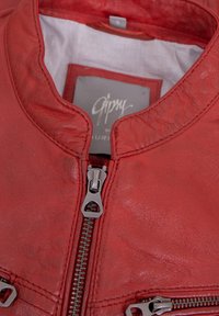 Rote Lederjacke mit Stehkragen, ausgestattet mit silbernen Reißverschlüssen und detaillierter Naht. Weiche Textur und glatte Oberfläche. Etikett im Kragen.