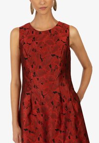 Rotes ärmelloses Kleid mit einem strukturierten Blumenmuster, das schwarze Akzente und eine taillierte Silhouette aufweist. Mit seitlichen Taschen.