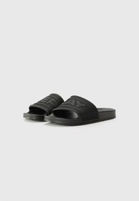Black rubber slide sandals with textured straps, featuring raised letters and a flat sole. Design is minimalistic with open-toe structure.