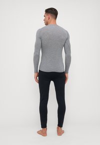 Šedé triko s dlouhým rukávem a přiléhavým střihem, kombinované s černými slim-fit kalhotami. Tričko má jemnou texturu a kulatý výstřih.