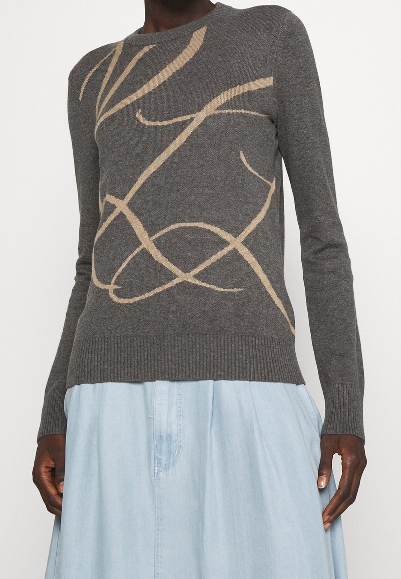 Pull gris foncé avec des motifs abstraits en spirale beige clair, porté avec une jupe bleu clair, manches longues, ourlet et poignets côtelés.
