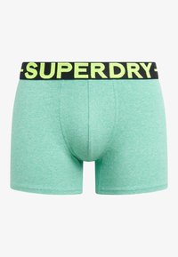 Bóxers mint verdes con una cinturilla elástica negra que presenta "SUPERDRY" en letras amarillas vibrantes. Material suave y elástico.
