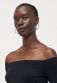 Svart av-og-shoulder topp laget av mykt stoff, med en tettsittende design og glatt tekstur, med rett halslinje og brede ermer.