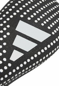 Producto textil negro que presenta patrones texturizados y acentos blancos con puntos. Un logotipo blanco destacado con formas triangulares se exhibe de manera prominente.
