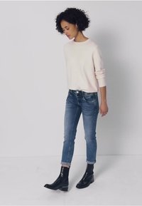 Ljusrosa tröja, blå jeans med uppvikta muddar och svarta ankelboots. Fokus på tygstruktur och avslappnad passform.