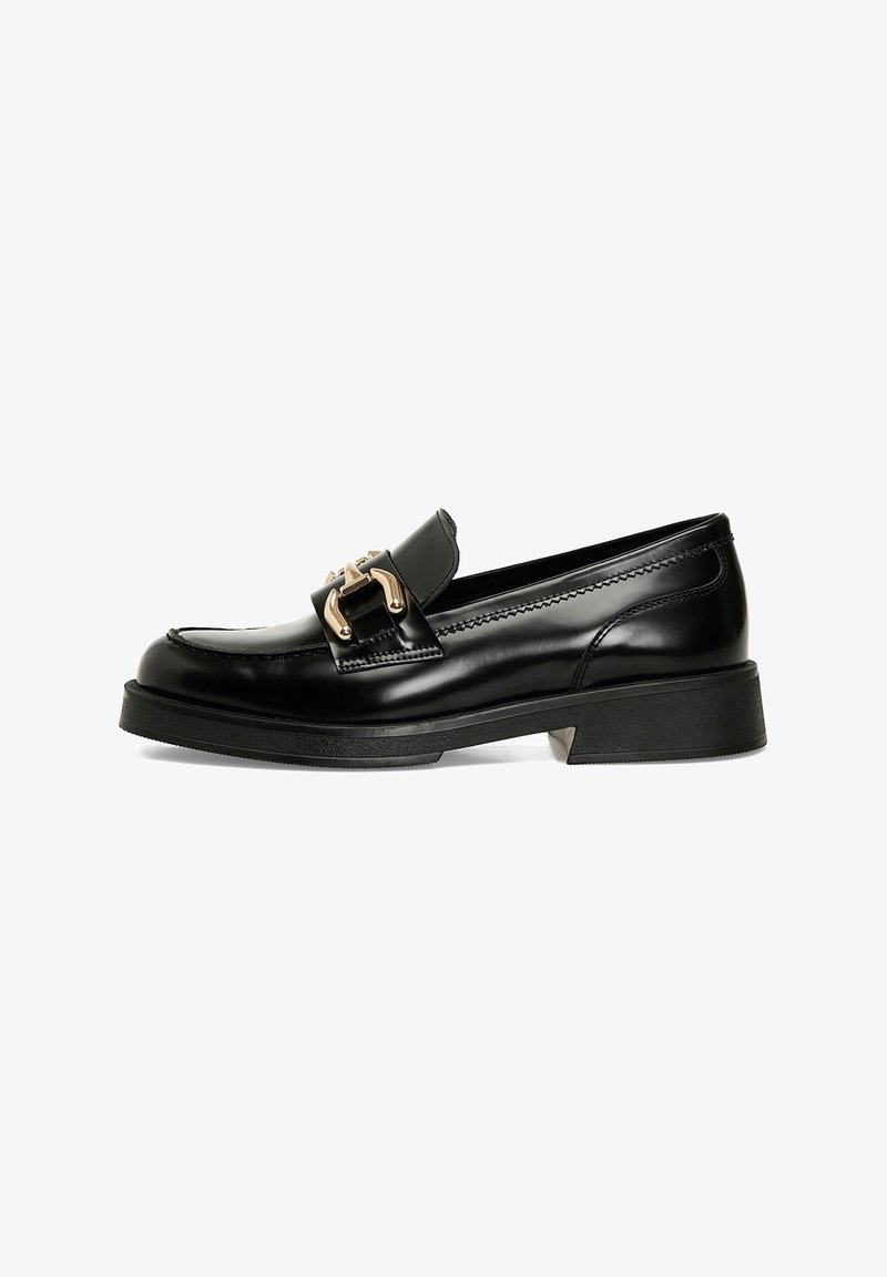 Mocassino in pelle nera con una fibbia decorativa dorata. Presenta una superficie liscia, punta arrotondata e un tacco basso a blocco con suola textured.