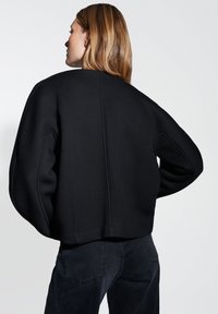 Maglione nero oversize con un collo alto, spalle cadenti e una texture morbida. La parte posteriore presenta una cucitura centrale, offrendo una vestibilità comoda.