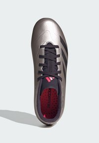 Zapatilla de fútbol gris con acabado brillante, acentos negros y upper texturizado. Cuenta con cordones y un forro interior rojo con agujeros de ventilación.